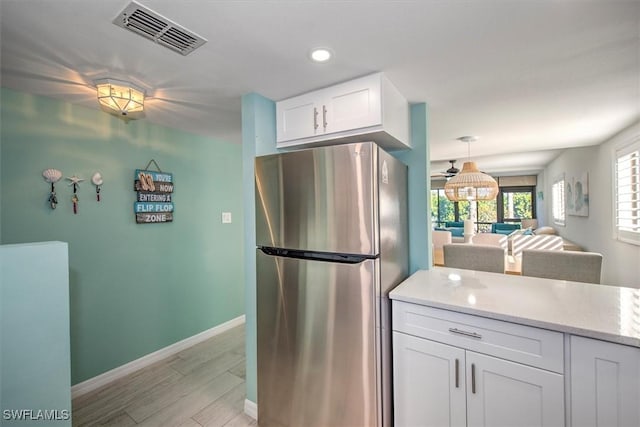 kitchen featuring white cabinetry, hanging light fixtures, light stone counters, stainless steel fridge, and light wood-type flooring