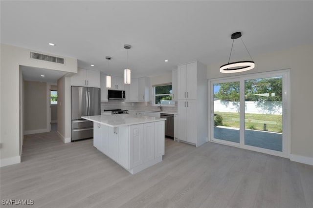 kitchen with appliances with stainless steel finishes, white cabinets, hanging light fixtures, and a center island