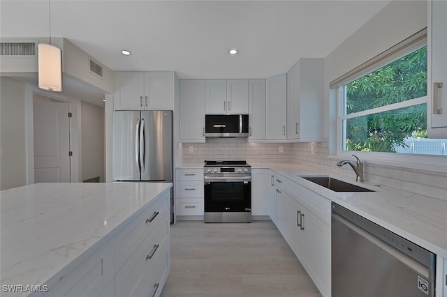 kitchen with appliances with stainless steel finishes, hanging light fixtures, light stone countertops, sink, and white cabinetry