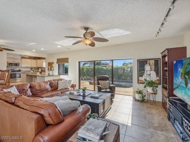 living room with a textured ceiling, ceiling fan, light tile patterned floors, and track lighting