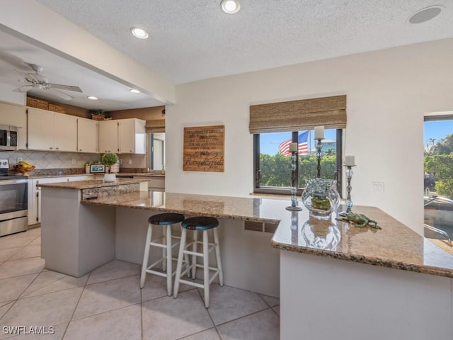 kitchen with light stone counters, light tile patterned flooring, a textured ceiling, and appliances with stainless steel finishes