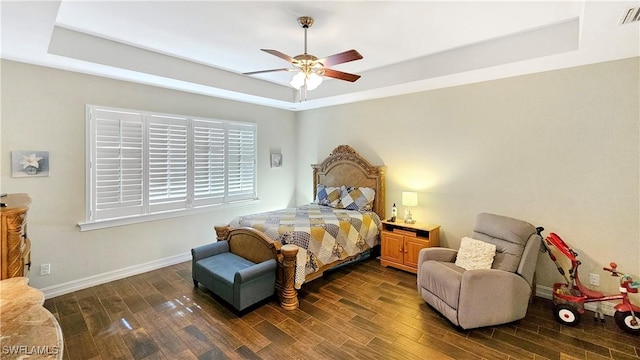 bedroom with a tray ceiling, dark wood-style flooring, visible vents, and baseboards