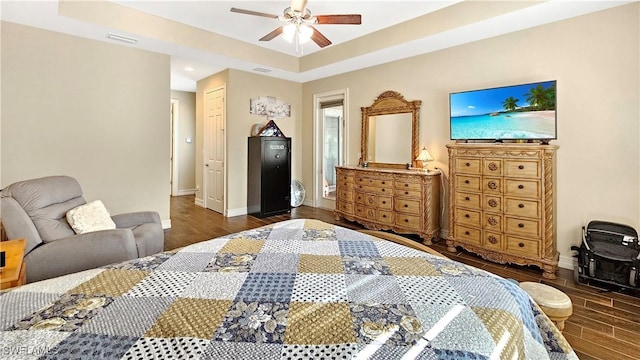 bedroom featuring visible vents, baseboards, a tray ceiling, and wood finished floors