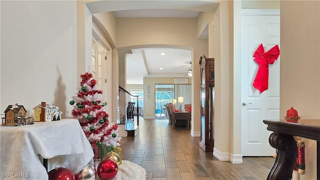 hallway with wood finish floors, arched walkways, recessed lighting, stairway, and baseboards