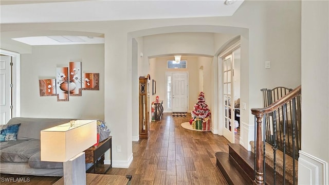 entryway with arched walkways, wood finished floors, and baseboards