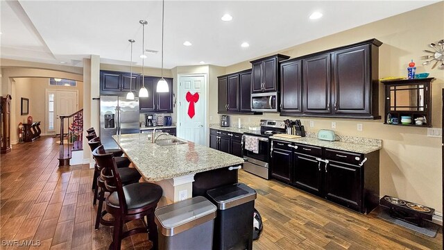 kitchen with pendant lighting, dark wood finished floors, stainless steel appliances, a sink, and a kitchen bar