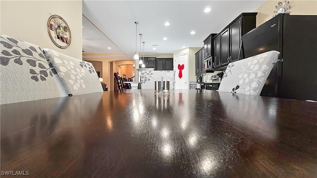 kitchen featuring arched walkways, recessed lighting, dark cabinets, freestanding refrigerator, and stainless steel microwave