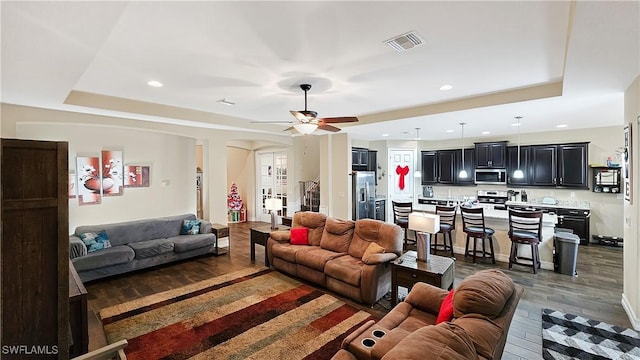 living area featuring visible vents, arched walkways, a raised ceiling, stairway, and wood finished floors