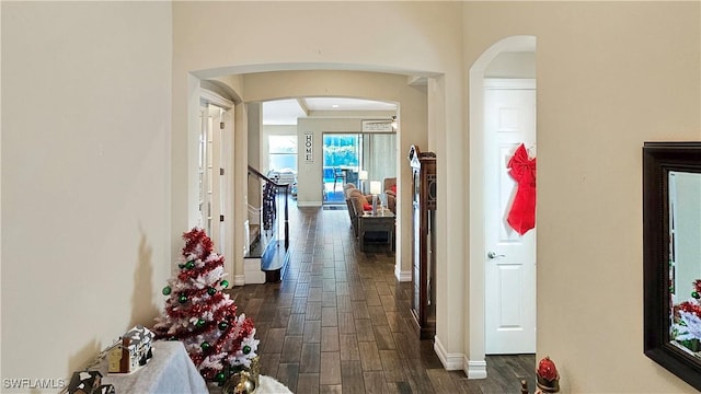 corridor featuring dark wood-style floors, baseboards, and arched walkways