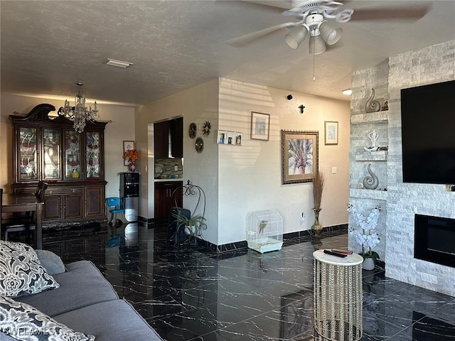 living room with ceiling fan with notable chandelier, a textured ceiling, and a stone fireplace