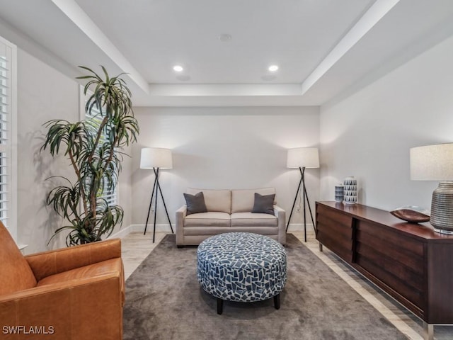 living area with recessed lighting, a raised ceiling, and baseboards