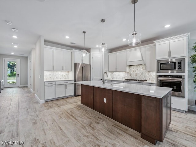 kitchen featuring white cabinets, stainless steel appliances, light countertops, premium range hood, and a sink