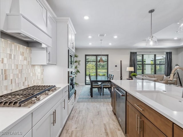 kitchen featuring custom exhaust hood, white cabinets, sink, light wood-type flooring, and appliances with stainless steel finishes