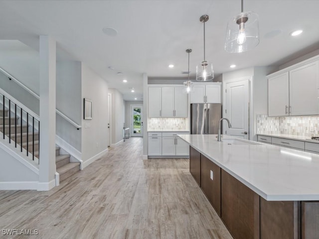 kitchen featuring stainless steel refrigerator, white cabinetry, sink, pendant lighting, and light wood-type flooring