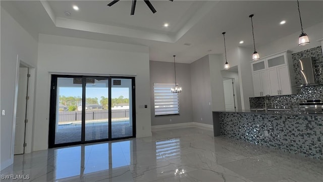 kitchen with wall chimney exhaust hood, a raised ceiling, backsplash, decorative light fixtures, and white cabinets