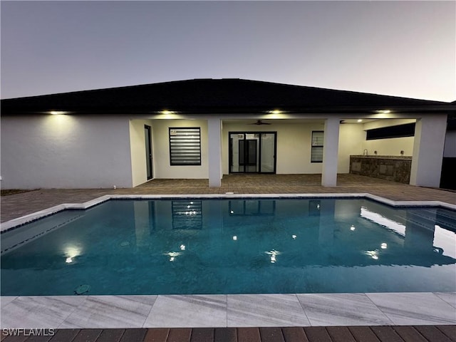 pool at dusk with ceiling fan and a patio area