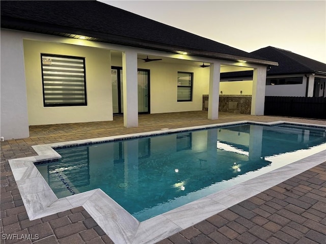 pool at dusk featuring ceiling fan and a patio