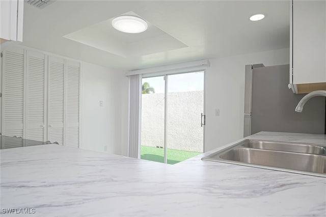 kitchen featuring white cabinets, stainless steel fridge, sink, and a tray ceiling