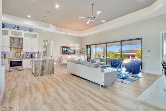 living room featuring a towering ceiling, ceiling fan with notable chandelier, light hardwood / wood-style flooring, and a raised ceiling