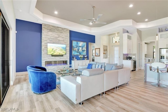 living room featuring a raised ceiling, a tiled fireplace, ceiling fan, and light hardwood / wood-style flooring