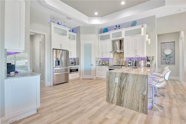 kitchen with light stone countertops, wall chimney exhaust hood, stainless steel appliances, sink, and white cabinetry