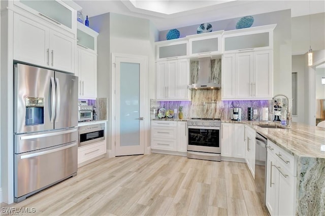 kitchen with light stone countertops, wall chimney exhaust hood, stainless steel appliances, white cabinetry, and hanging light fixtures