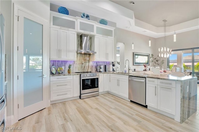 kitchen with appliances with stainless steel finishes, decorative light fixtures, white cabinetry, and wall chimney range hood