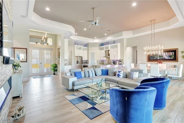 living room featuring a raised ceiling, french doors, and ceiling fan with notable chandelier