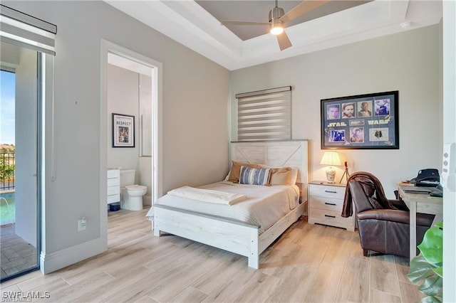 bedroom featuring ceiling fan, light hardwood / wood-style flooring, ensuite bathroom, a tray ceiling, and access to outside