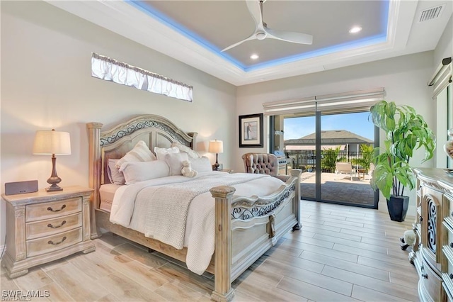 bedroom with ceiling fan, access to exterior, and a tray ceiling