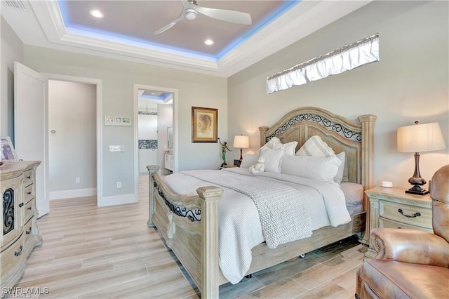 bedroom with a tray ceiling, ensuite bathroom, ceiling fan, and light wood-type flooring