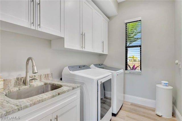 clothes washing area with washer and dryer, light hardwood / wood-style floors, cabinets, and sink