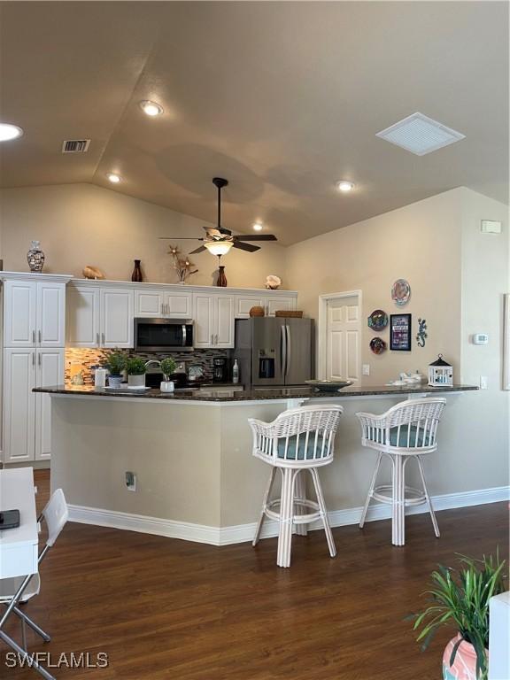 kitchen featuring white cabinetry, dark hardwood / wood-style flooring, backsplash, vaulted ceiling, and appliances with stainless steel finishes