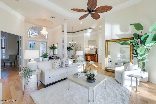 living room featuring a towering ceiling, ornamental molding, ceiling fan with notable chandelier, and light wood-type flooring