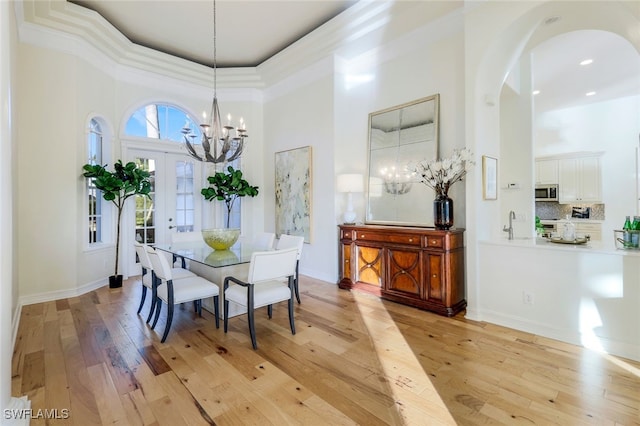 dining room with crown molding, light hardwood / wood-style floors, a high ceiling, and a notable chandelier