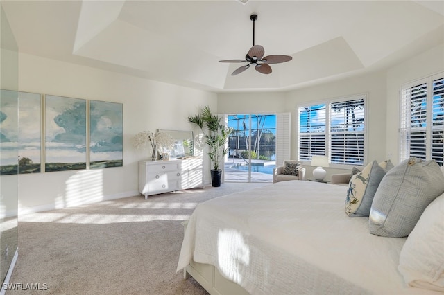 carpeted bedroom featuring a tray ceiling, access to exterior, and ceiling fan