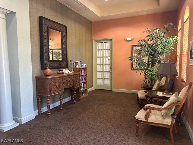 sitting room with a raised ceiling, ornate columns, and dark colored carpet