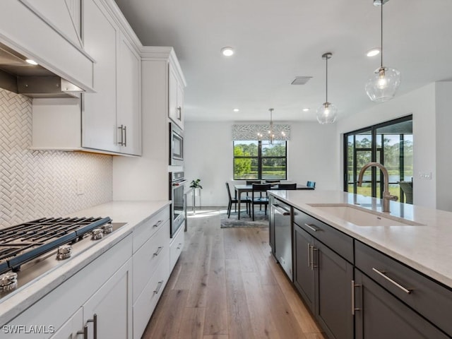 kitchen with premium range hood, stainless steel appliances, sink, pendant lighting, and white cabinetry