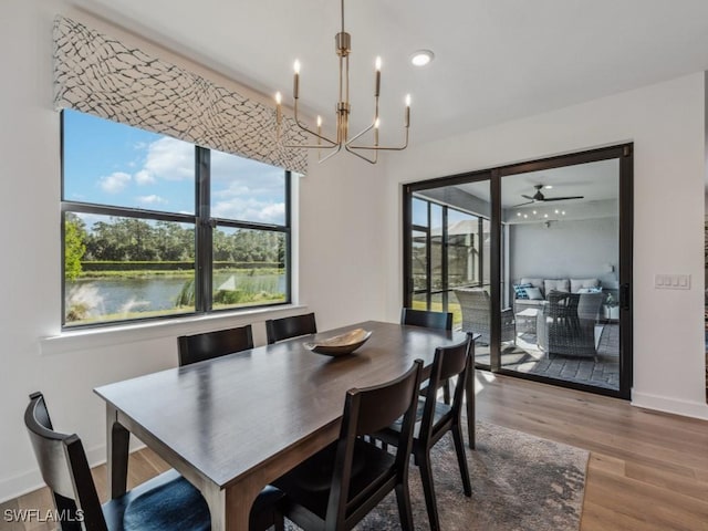 dining space featuring a water view, wood-type flooring, and ceiling fan with notable chandelier