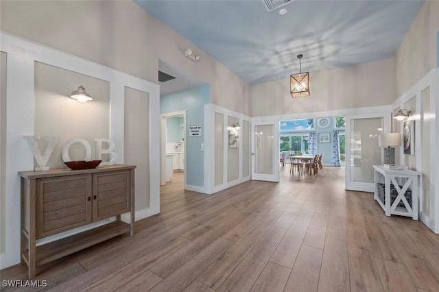 foyer entrance featuring french doors, light hardwood / wood-style floors, a high ceiling, and an inviting chandelier