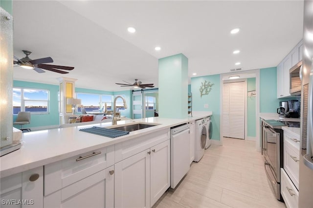 kitchen with washing machine and clothes dryer, white cabinetry, sink, ceiling fan, and appliances with stainless steel finishes