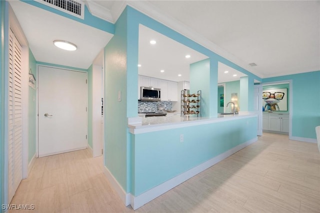 interior space featuring light wood finished floors, visible vents, baseboards, ornamental molding, and a sink