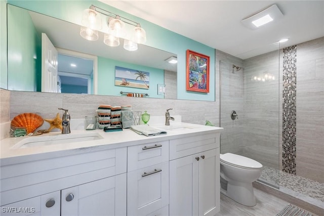 bathroom with a tile shower, wood-type flooring, toilet, vanity, and tile walls