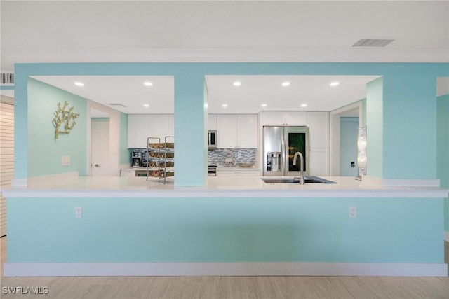 kitchen with sink, kitchen peninsula, appliances with stainless steel finishes, white cabinets, and light wood-type flooring