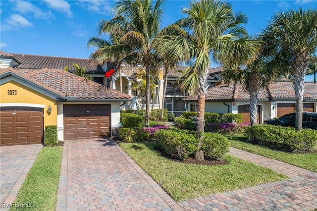 view of front facade with decorative driveway, a tiled roof, an attached garage, and stucco siding