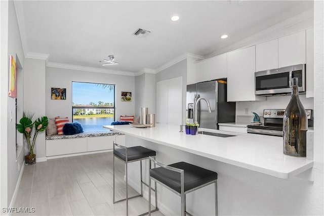 kitchen featuring crown molding, visible vents, appliances with stainless steel finishes, white cabinetry, and a kitchen breakfast bar