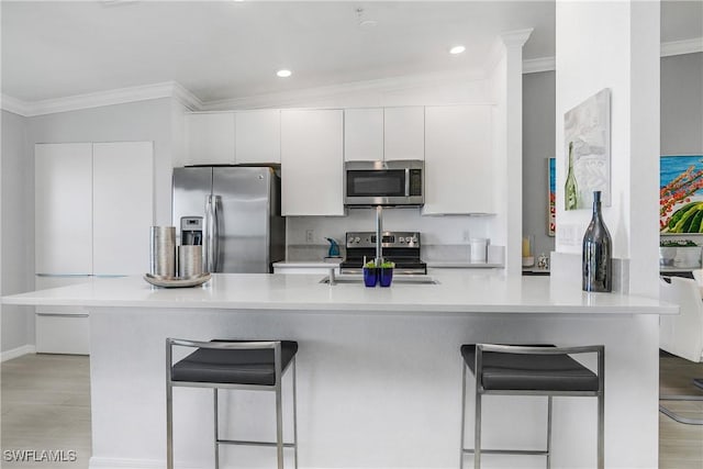 kitchen featuring stainless steel appliances, a breakfast bar, white cabinets, light countertops, and crown molding