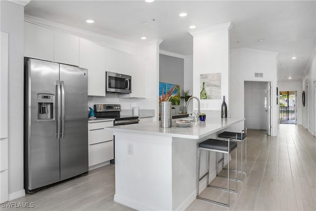 kitchen featuring light countertops, appliances with stainless steel finishes, white cabinets, a sink, and a kitchen breakfast bar