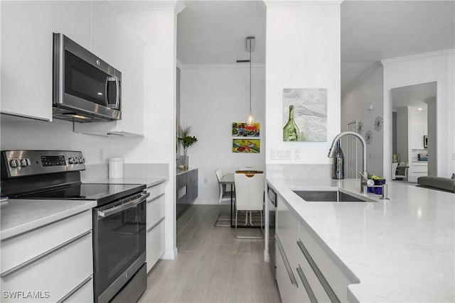 kitchen with white cabinets, modern cabinets, appliances with stainless steel finishes, ornamental molding, and a sink