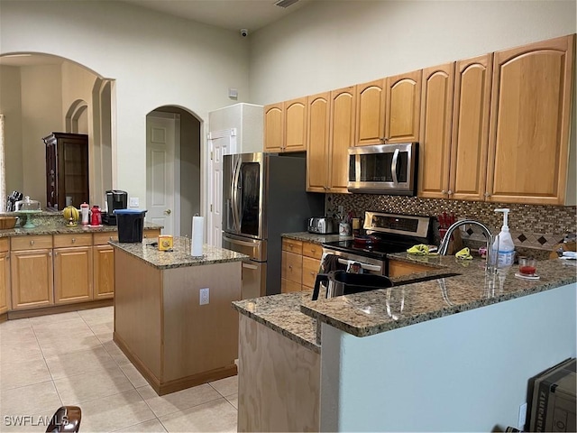 kitchen featuring stone counters, appliances with stainless steel finishes, a center island, and kitchen peninsula